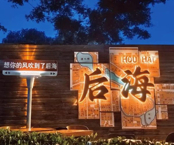 Night scene of a wooden wall with an illuminated map-marts art piece featuring large glowing Chinese characters, against a dark blue evening sky. or Wooden wall installation with a lit multi-panel map and big illuminated Chinese characters, in a nighttime setting.