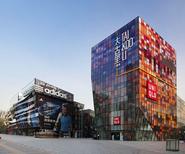 Taikoo Li Sanlitun, Beijing, chinatravel, Colorful glass shopping complex with Uniqlo storefronts, adjacent Adidas billboard, under a clear blue sky in daytime.