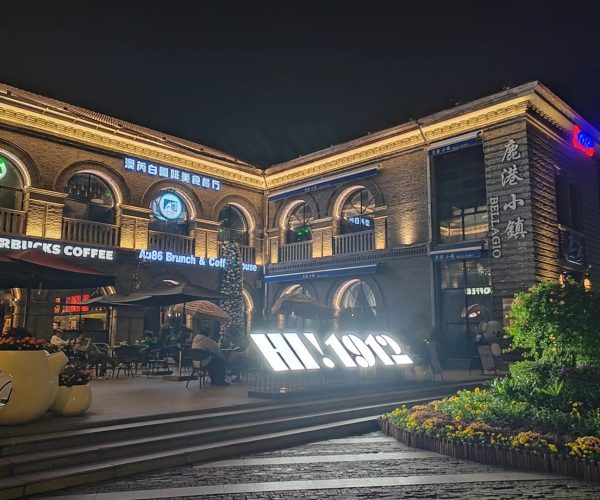 1912 Street,Nanjing,China tour Night view of a brick two-story building with arched windows, warm lights, and outdoor cafe seating, including a Starbucks sign.