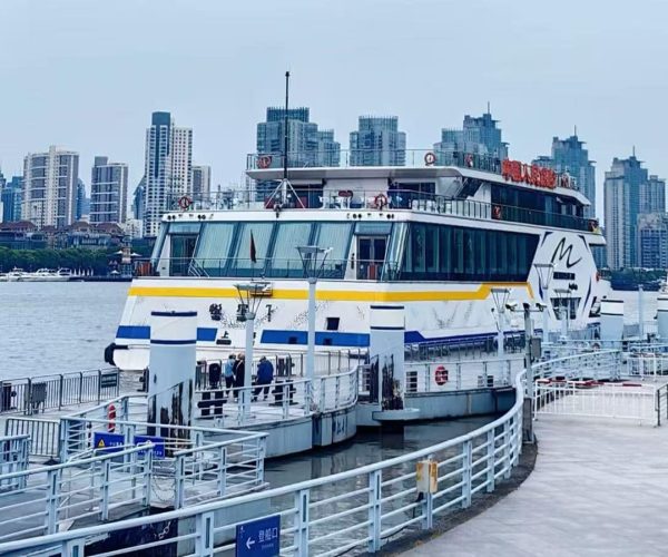 Huangpu River,Shanghai,Chinatour Passenger ferry docked at a marina, with glass-walled decks and a yellow stripe, against a skyline of tall buildings across the water.