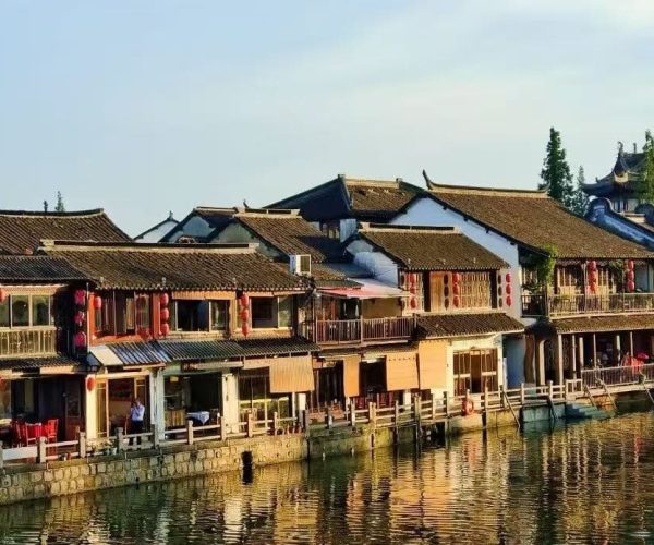 Zhujiajiao Water Town,Shanghai,Chinatour Traditional riverside street of two-story wooden buildings with tiled roofs, red lanterns, and balconies along a calm canal.