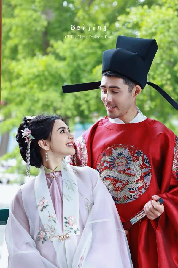 Hanfu photoshoot, Beijing, zhongshan park, couple, chinatravel, Couple in traditional Chinese wedding attire outdoors: man in red dragon-embroidered robe and tall black hat, woman in pale floral hanfu smiling at him.