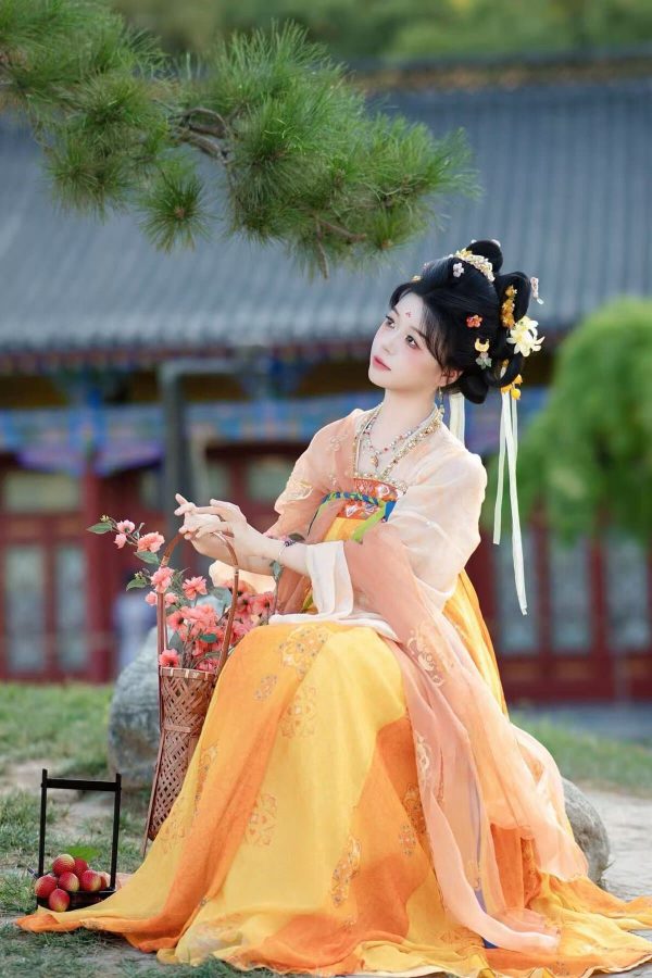 Hanfu photoshoot, xingqing palace, xi'an, solo, tang dynasty, female, chinatravel, Woman in peach-and-yellow traditional Hanfu with ornate hair pieces sits outdoors, holding a flower basket beside pink blossoms and apples on the ground.