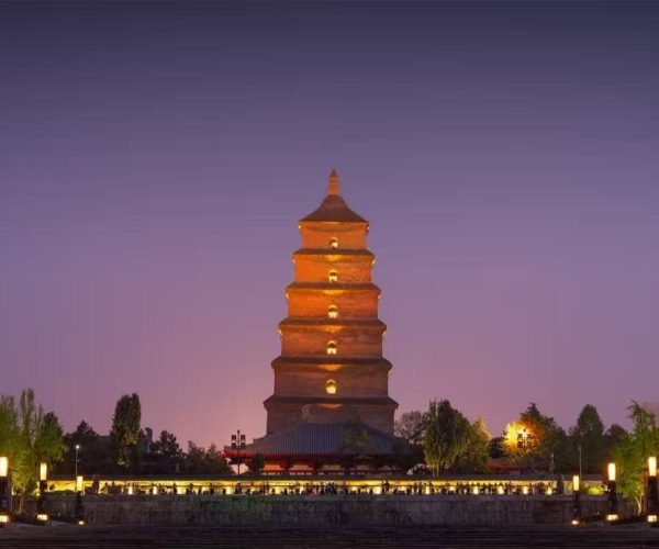Five-story brick pagoda glowing orange at night, surrounded by trees and a lantern-lit plaza.
