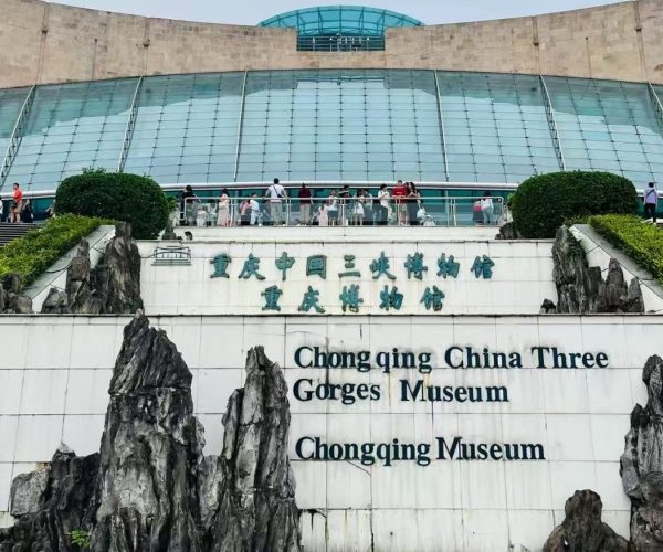 Chongqing Three Gorges Museum,Chongqing,Chinatour Exterior view of Chongqing China Three Gorges Museum with a glass-domed atrium, visitors on the terrace, and rock sculptures framing a sign that reads 'Chongqing China Three Gorges Museum' in English and Chinese.