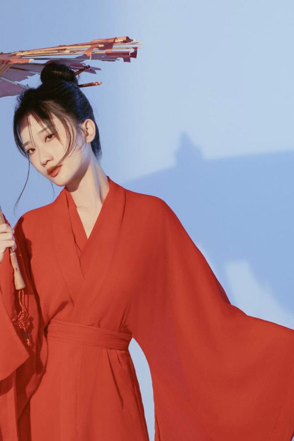 Xi’an Hanfu Photoshoot with Beautiful origami umbrella, chinatrip, Woman in a red traditional robe holding a pink parasol, posing outdoors against a blue sky.