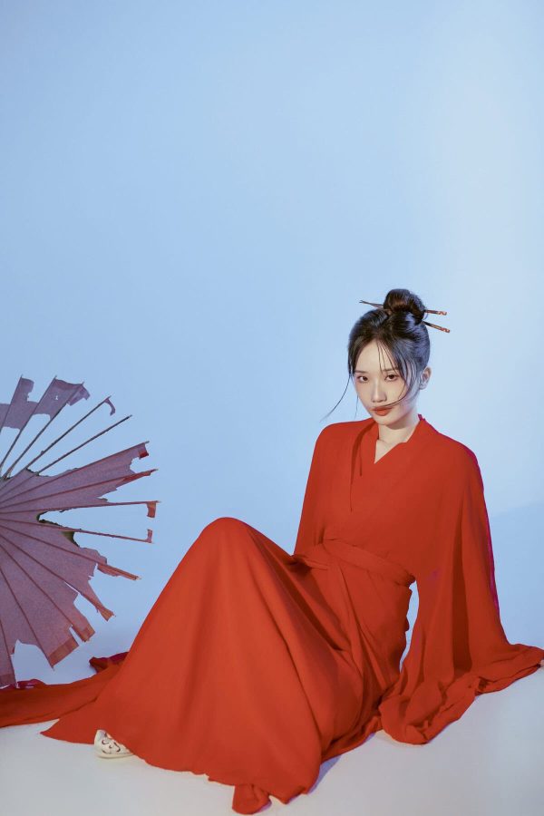 Hanfu Photoshoot, chinese traditonal dress-up, beijing, china tour, Woman in a flowing red dress seated on the floor against a pale blue backdrop, with a torn purple parasol resting nearby on the left.
