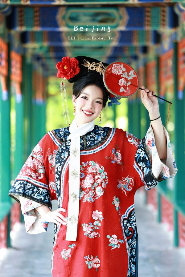 hanfu photoshoot, the forbidden city, beijing, qing dynasty, female, solo, chinatravel, Woman in a bright red, embroidered traditional Chinese dress and elaborate headdress, holding a red floral fan in a colorful temple corridor.