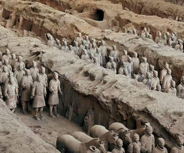 Row of life-sized terracotta soldiers emerging from an excavation pit in China.