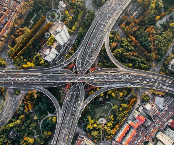 transportation, Chengdu, Chinatravel, Aerial view of an intricate urban highway interchange with looping ramps and heavy traffic, surrounded by autumn-colored trees while buildings line the edges.