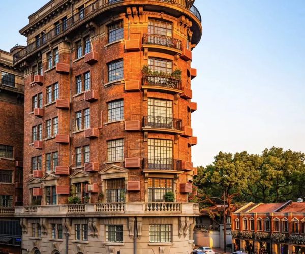Corner brick residential building with curved corner and multiple balconies on a busy city street at sunset.