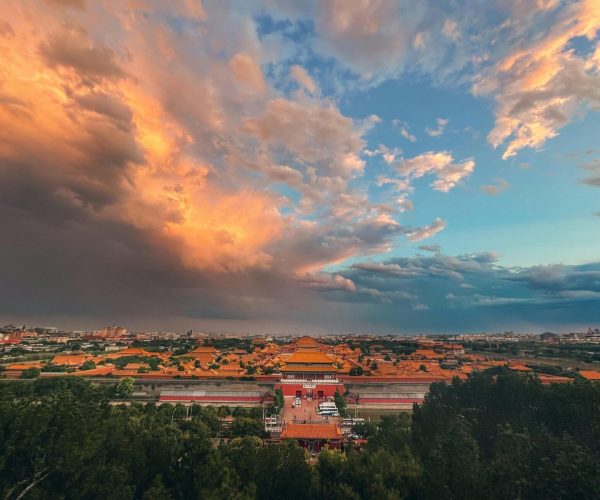 Jingshan Park Panoramic view, Beijing, Chinatrave, Aerial view of a city with rows of orange-tiled rooftops and a dramatic sunset sky with orange clouds above.