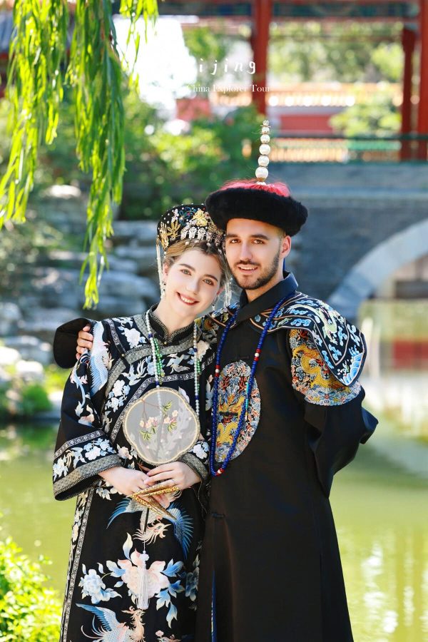 hanfu photoshoot, zhongshan park, beijing, couple, chinatrip, Smiling couple in traditional Chinese wedding attire outdoors, the woman holding a round embroidered fan beside the groom by a pond.",