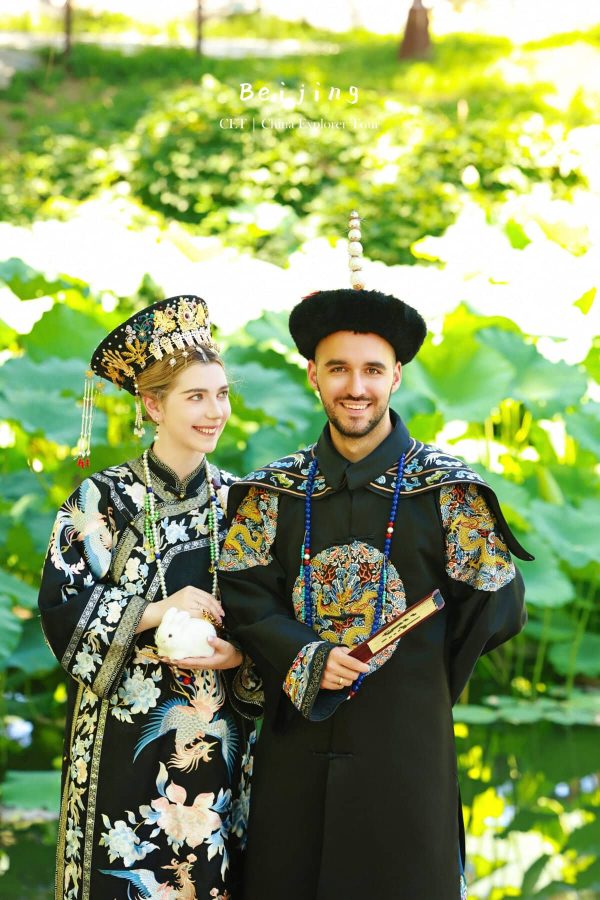 hanfu photoshoot, zhongshan park, beijing, couple, chinatrip, Smiling couple in elaborate traditional Chinese wedding attire posing outdoors in a lush garden setting.