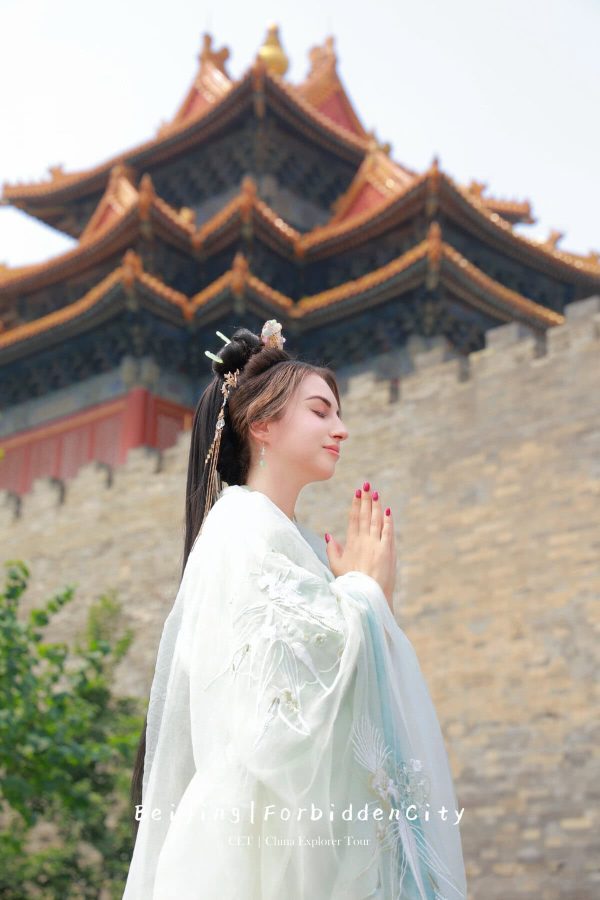 hanfu photoshoot, the forbidden city, beijing, female, solo, chinatravel, Woman in a pale traditional Hanfu praying with hands pressed together in front of Beijing's Forbidden City roofed architecture behind her.