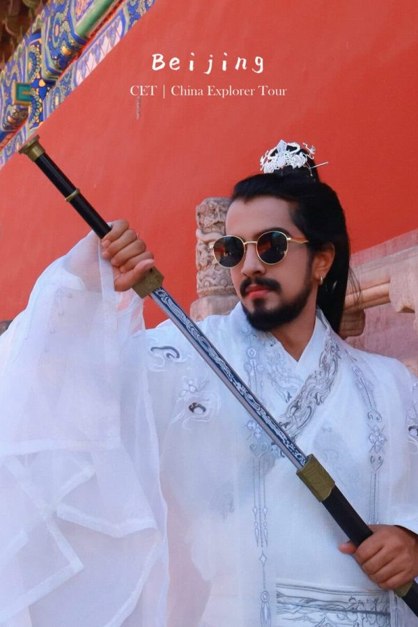Hanfu photoshoot, Beijing, Imperial Ancestral Temple (Tai Miao), male, chinatravel, Man in white ceremonial robes with a sword, wearing a small crown and round sunglasses, posing in front of a red temple wall with ornate stone railing.