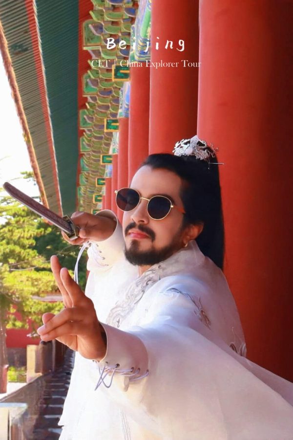hanfu photoshoot, the forbidden city, beijing, male, solo, chinatravel, Man in white traditional attire with tiara and sunglasses poses with a sword at a red temple wall.