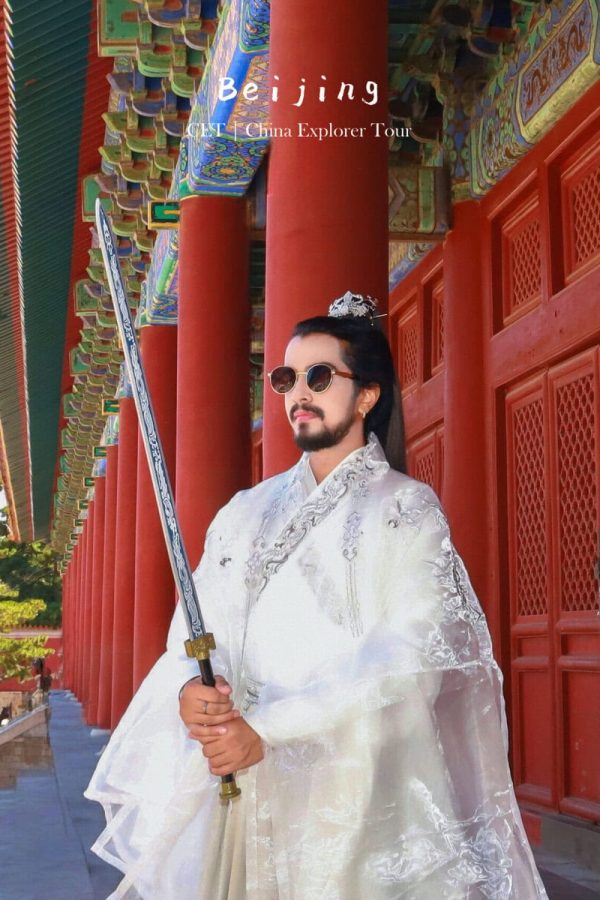 hanfu photoshoot, the forbidden city, beijing, male, solo, chinatravel, Man in a white ceremonial robe with a sword, standing beside red pillars at a colorful Chinese temple in Beijing.