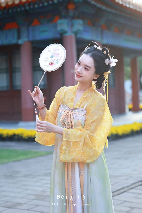 Hanfu photoshoot, the forbidden city, beijing, chinatravel, Woman in a yellow Hanfu holding a round floral fan, standing in a temple courtyard with ornate architecture in the background.