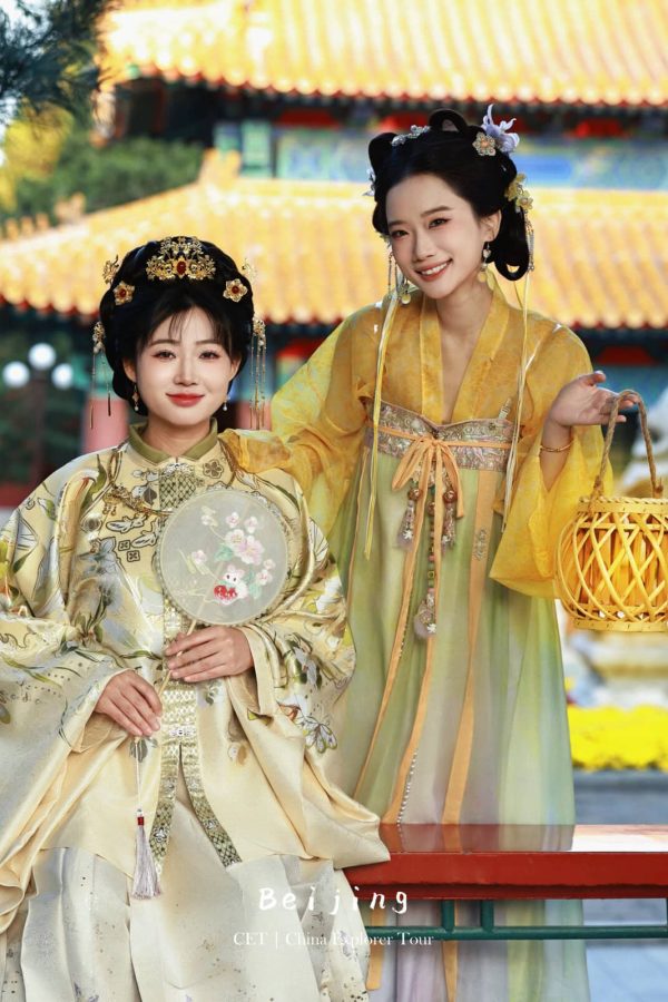 Hanfu photoshoot, the forbidden city, beijing, chinatravel, Two women in ornate yellow and cream traditional Chinese hanfu stand in a sunlit temple courtyard; one holds a delicate fan while the other carries a woven lantern and smiles at the camera.