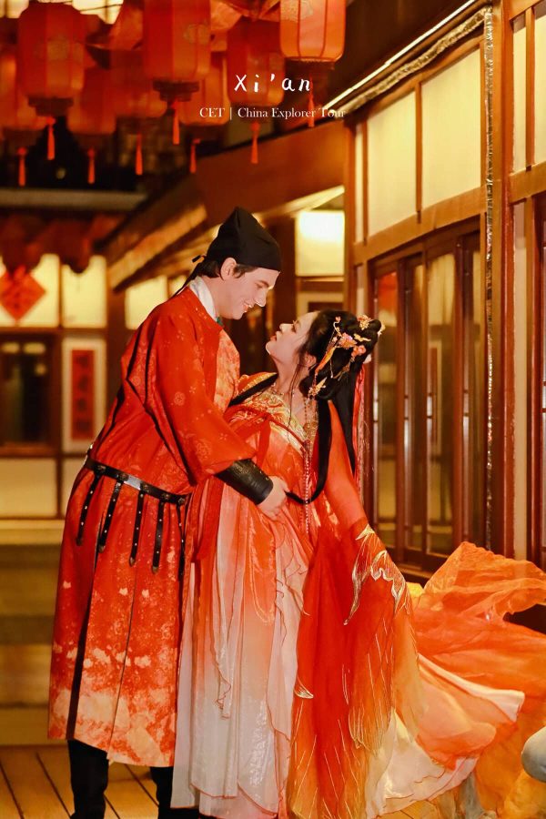 Hanfu photoshoot, xi'an, xingqing palace couple, chinatravel, Couple in red traditional Chinese wedding attire sharing a smile indoors among hanging red lanterns.