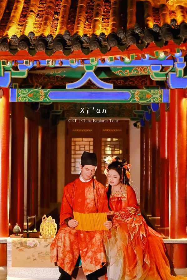 Hanfu photoshoot, xi'an, xingqing palace couple, chinatravel, Couple in red traditional Chinese wedding attire standing in a colorful temple doorway.