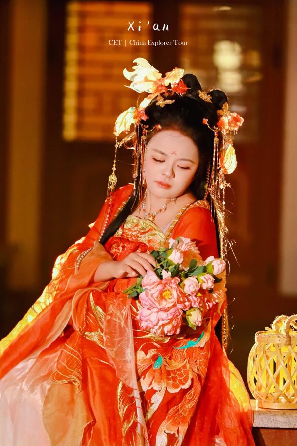 Hanfu photoshoot, zhongshan park, beijing, solo, tang dynasty, female, chinatravel, Woman in ornate red and orange traditional Chinese dress with a floral headdress, gazing at a pink bouquet she holds.