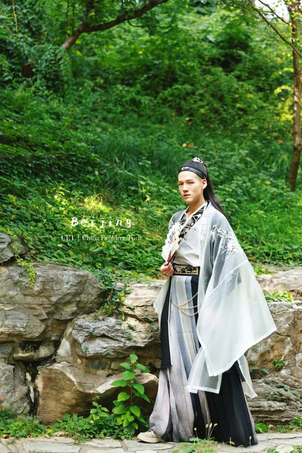 Hanfu Photoshoot, Beijing, zhongshan park, male, chinatravel, Person in traditional Chinese hanfu standing beside rocks in a lush garden, with Beijing travel text overlaid.