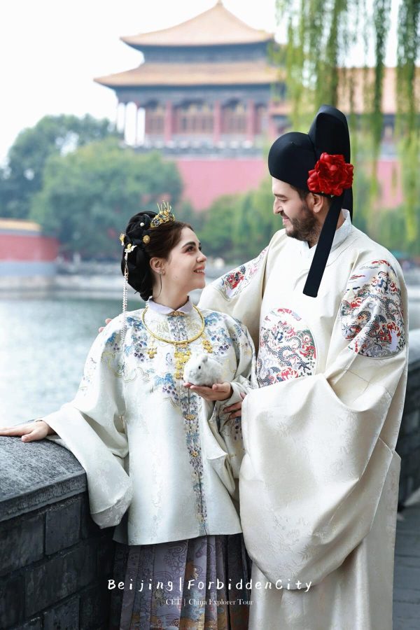 Hanfu photoshoot, Beijing, forbidden city exterior, couple, chinatravel, Couple in ornate traditional Chinese wedding robes smiling at each other beside a stone railing by water, with a historic Beijing temple in the background.