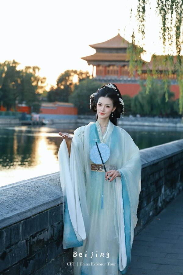 Hanfu photoshoot, Beijing, forbidden city exterior, female, chinatravel, Woman in a pale blue traditional Hanfu with ornate hairpieces stands on a riverside walkway in Beijing, pavilion visible in the background at sunset.