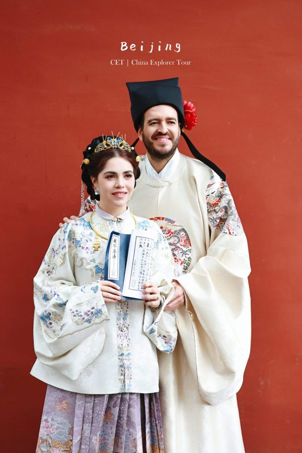 Hanfu photoshoot, Beijing, forbidden city exterior, couple, chinatravel, Couple in traditional Chinese wedding attire pose against a red wall, holding calligraphy scrolls and diplomas; Beijing/CET China Explorer Tour poster text above them