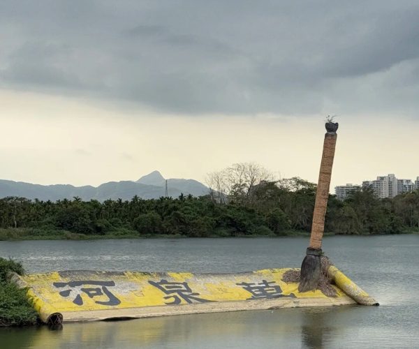 Wanquan River Scenic Area,Qionghai,Chinatravel Sunken yellow barge with black Chinese characters partially submerged in a lake; a tall tilted post with a bird nest sits on the right end, with trees and hills in the distance under cloudy skies.