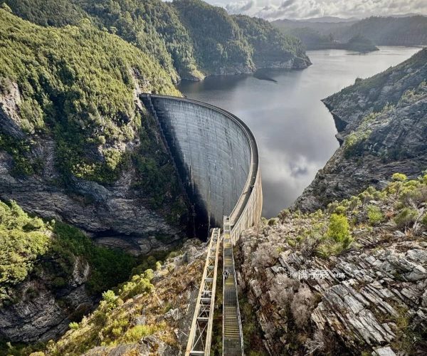 Three Gorges Dam Site,Yichang,Chinatravel Curved concrete dam spillway cutting through a rocky canyon with a calm reservoir and forested hills in the background.