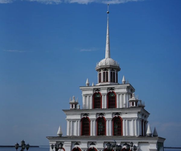 Sanjiangkou Ecological Tourism Area,Jiamusi,Chinatravel White multi-tiered seaside tower with red-trimmed windows and a tall spire under a blue sky.