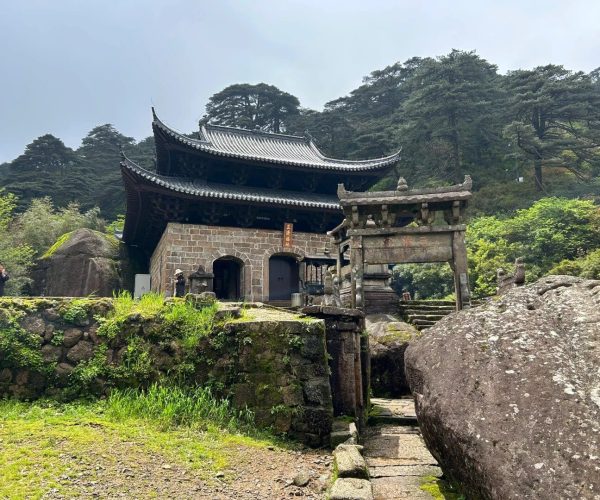 Sanqing Mountain Taoist Complex,Shangrao,Chinatrip Ancient East Asian temple with curved tiled roofs set on a stone base, surrounded by greenery in a forested mountain area.