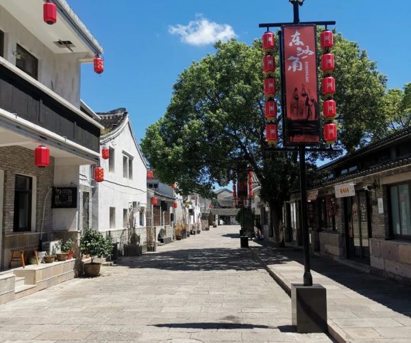 Dongsha Ancient Town,Zhoushan,Chinatravel Narrow pedestrian street in a traditional Chinese town, white buildings with red lanterns and a tall decorative sign against a blue sky.