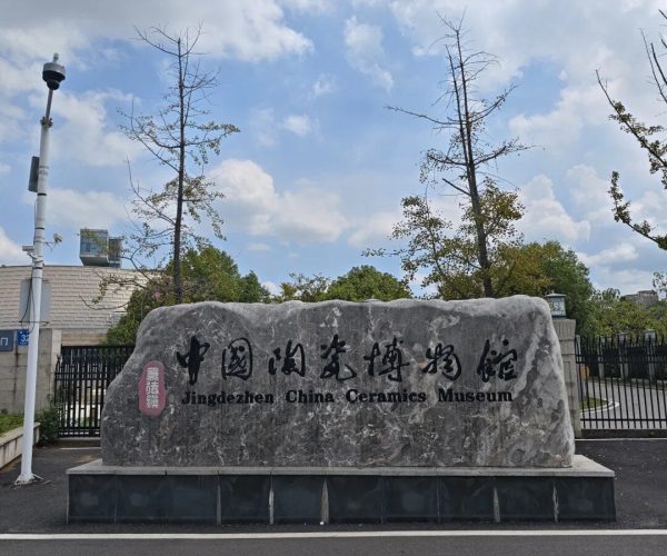 China Ceramic Museum,Jingdezhen,China tour Stone sign reading 'Jingdezhen China Ceramics Museum' at the museum entrance under a blue sky with trees and a gated fence in the background.