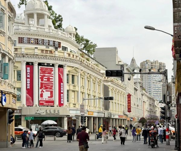 Zhongshan Road Pedestrian Street,Xiamen,Chinatravel Wide city street with white neoclassical buildings, red banners, and pedestrians crossing near shops.