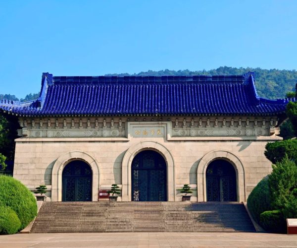 Sun Yat-sen Mausoleum,Nanjing,China tour Traditional Chinese building with a deep blue tiled roof, arched entrance doors, and stone steps flanked by greenery.
