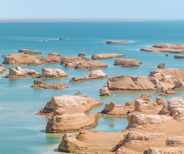 Wusute Water Yadan,Haixi Prefecture,China tour Coastal scene with numerous beige rocks jutting from turquoise waters under a clear blue sky toward a distant horizon.