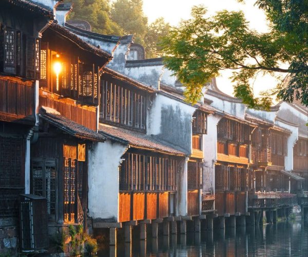 Wuzhen Water Town,Hangzhou,Chinatravel Traditional Chinese riverside houses on wooden stilts along a calm canal at sunset, reflecting golden light on the water