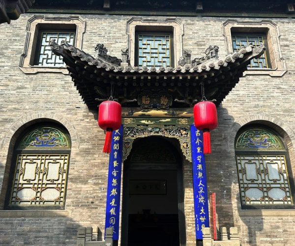 Qiao Family Courtyard Surroundings,Pingyao,Chinatravel Traditional Chinese temple entrance with ornate curved roof, blue couplets, and red lanterns hanging beside a stone staircase.
