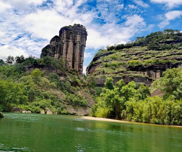Nine-Bend Stream ,Nanping,Chinatravel Tall rock formation rising from a forested riverbank under a blue sky with scattered clouds.