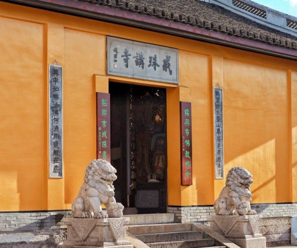 Hometown of the Sage of Calligraphy,Shaoxing,Chinatravel Orange temple entrance with two stone guardian lions on pedestals at the steps, Chinese plaques flanking the doorway and a blue sky above.
