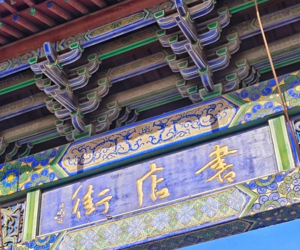 Bookstore Street，Kaifeng，Chinatravel Ornate Chinese temple arch with colorful beams, green and blue decorations, and a blue plaque with gold Chinese characters against a clear sky.