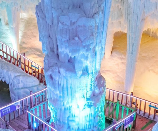 Yunqiu Mountain Ice Caves,Linfen,Chinatravel Ice cave interior with towering blue ice formations and a wooden walkway with railings nearby.