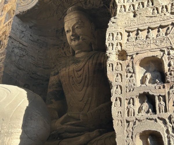 Yungang Grottoes,Datong,Chinatravel Large seated Buddha statue inside a rock-cut grotto, with a wall of small Buddha carvings along the right side.