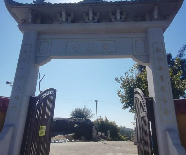 Yungu Temple,Huangshan,Chinatravel Ornate stone Chinese ceremonial arch (paifang) with dragon motifs, open double gates, sun behind, leading to a courtyard area.