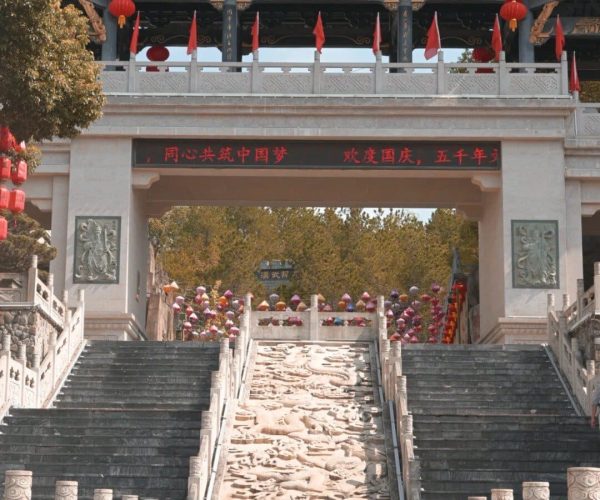 5000 Years Expo Park,Anqing,China tour Stone staircase with dragon-carved steps leading to a traditional Chinese gate adorned with red lanterns and flags.