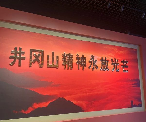 Jinggangshan Revolutionary Museum,Ji'an,China tour Red wall mural with golden Chinese characters reading '井冈山精神永放光芒' over a red sunset mountain landscape.